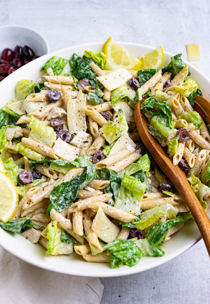 Close up angle shot of Caesar pasta salad with chicken with wooden serving spoons in the salad