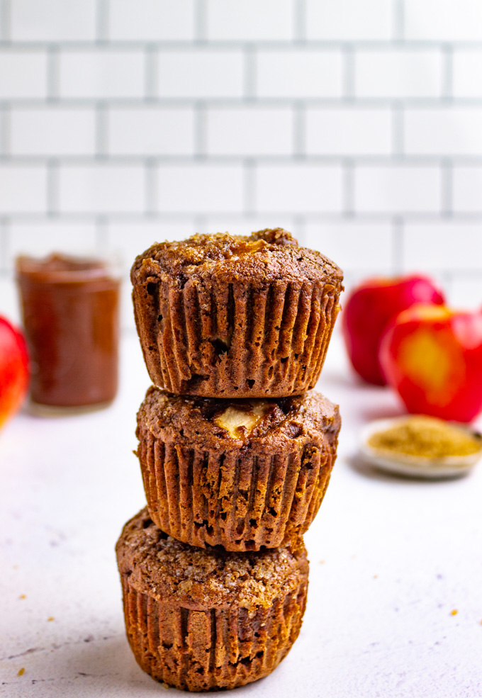 a stack of healthy apple butter muffins with apples in the background.