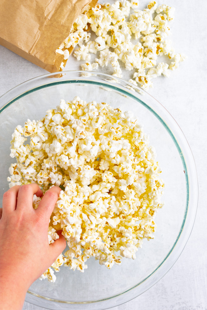popcorn in a glass mixing bowl with a hand reaching in to grab some