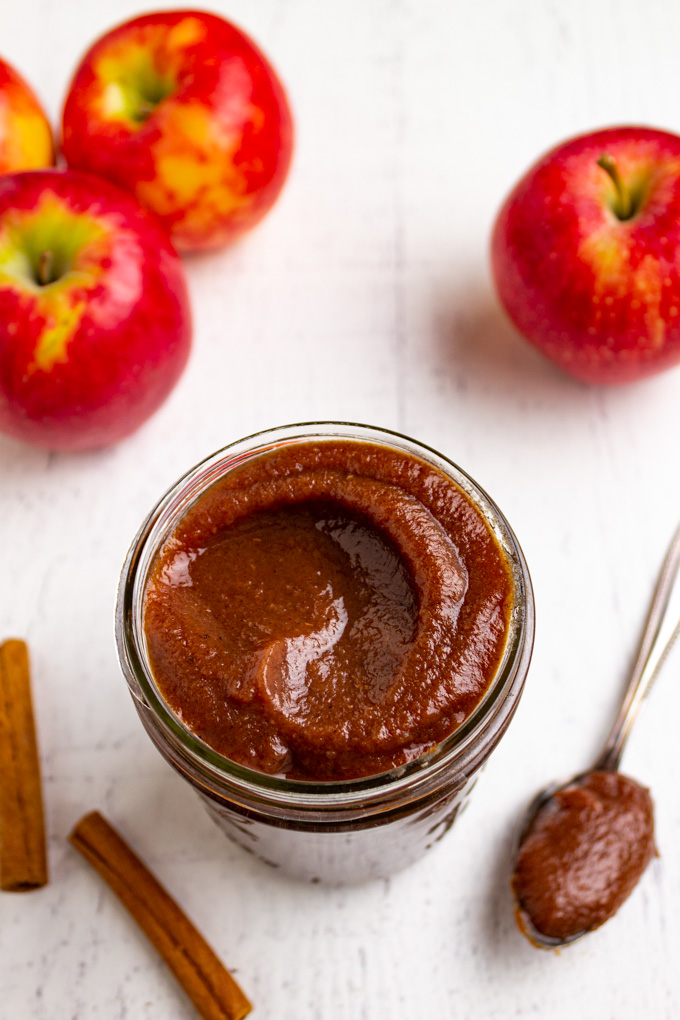 slow cooker apple butter in a jar with apples in the background.