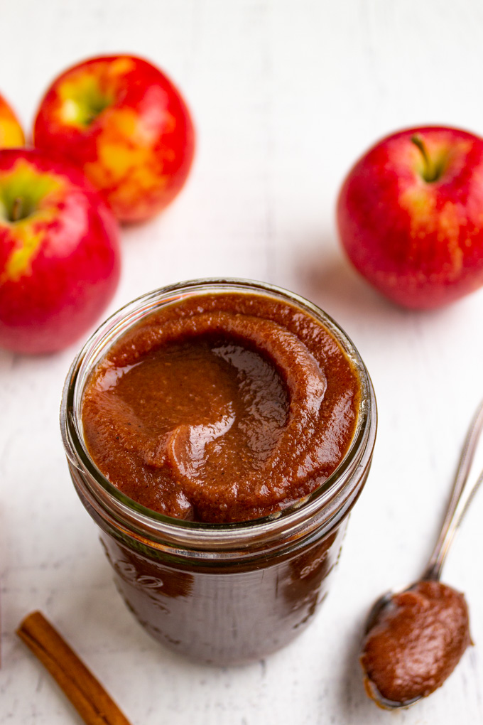 apple butter in a mason jar with a spoon and apples in the background.