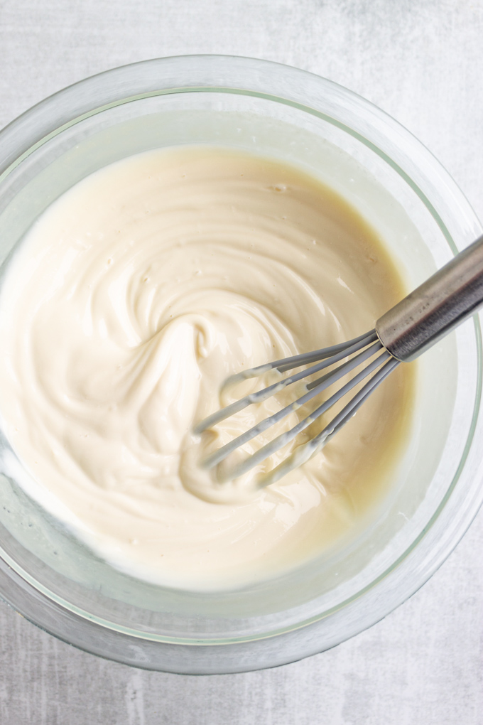 Greek yogurt topping in a mixing bowl, being stirred by a whisk.