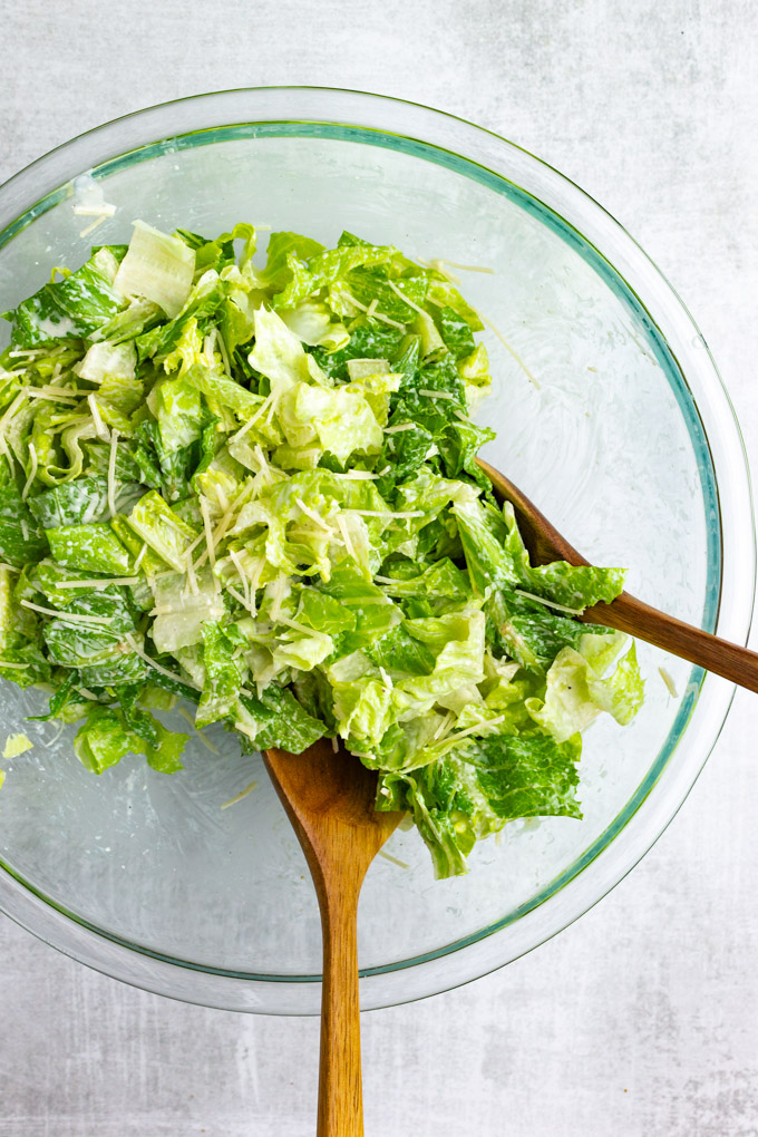 romaine lettuce being tossed with dressing, in a mixing bowl.