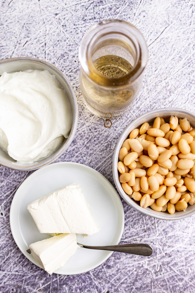 Ingredients in different bowls: cream cheese, Greek yogurt, white beans, and white wine. 