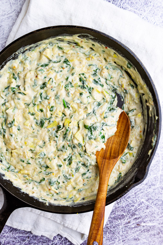 spinach artichoke dip in a cast iron skillet with a wooden spoon.