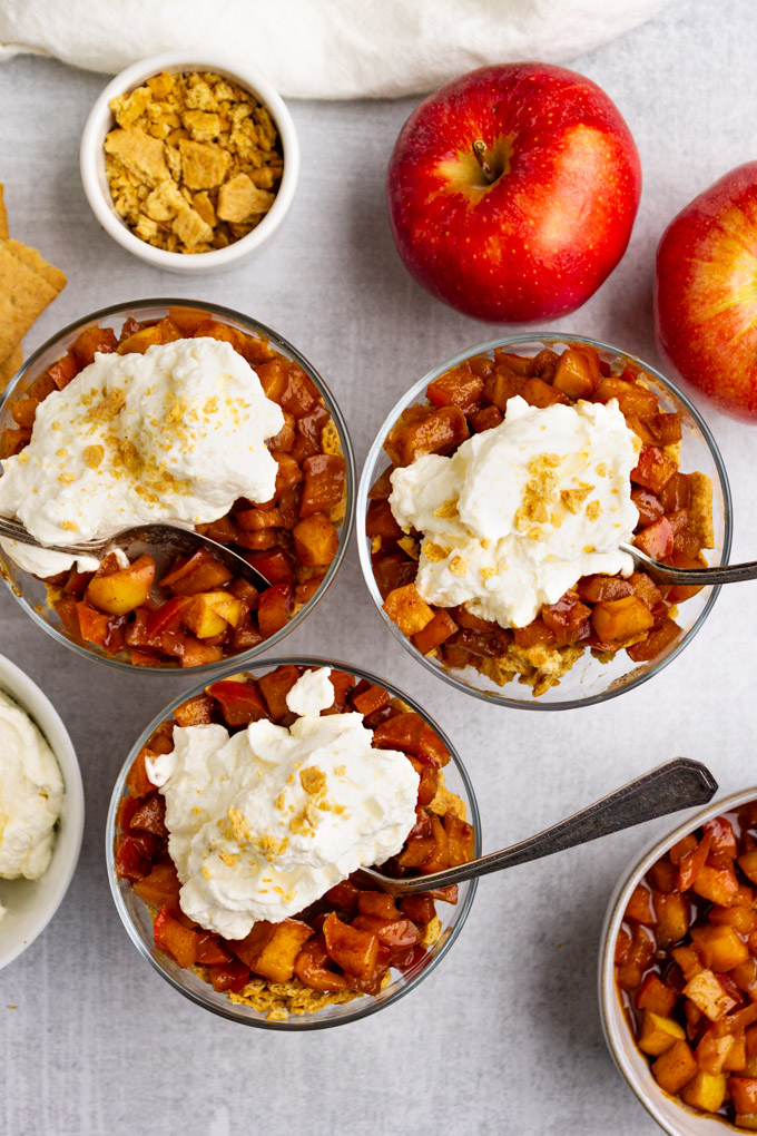 overhead shot of apple pie parfaits with dollops of whipped cream and spoons in each parfait.