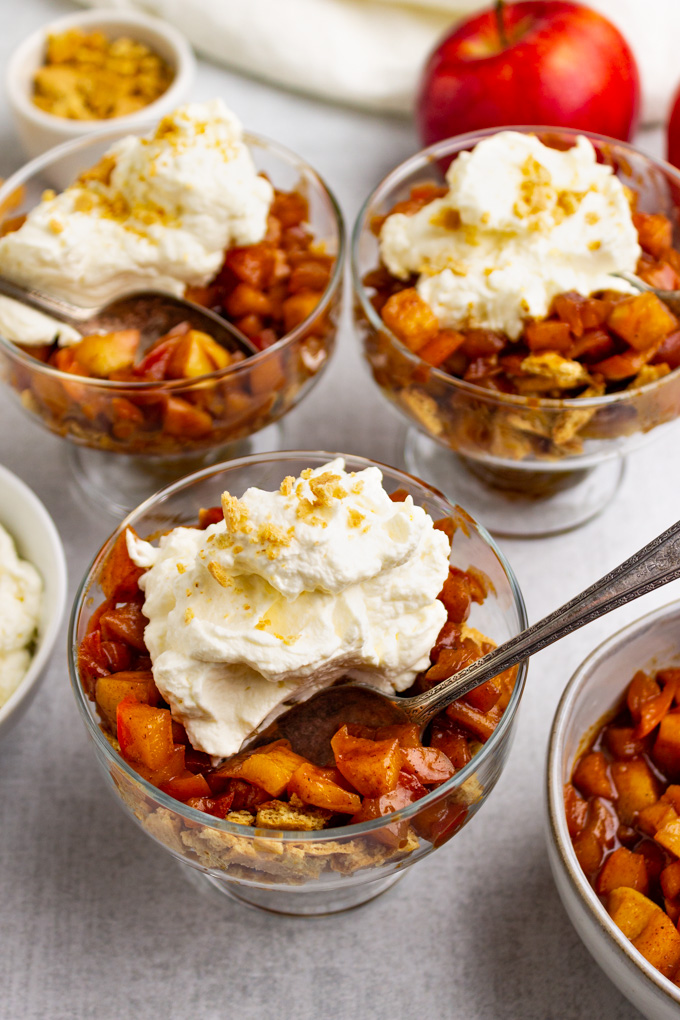 angled close up shot of apple pie parfaits topped with whipped cream.