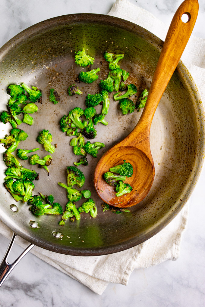 broccoli sautéed in a pan with a wooden spoon.