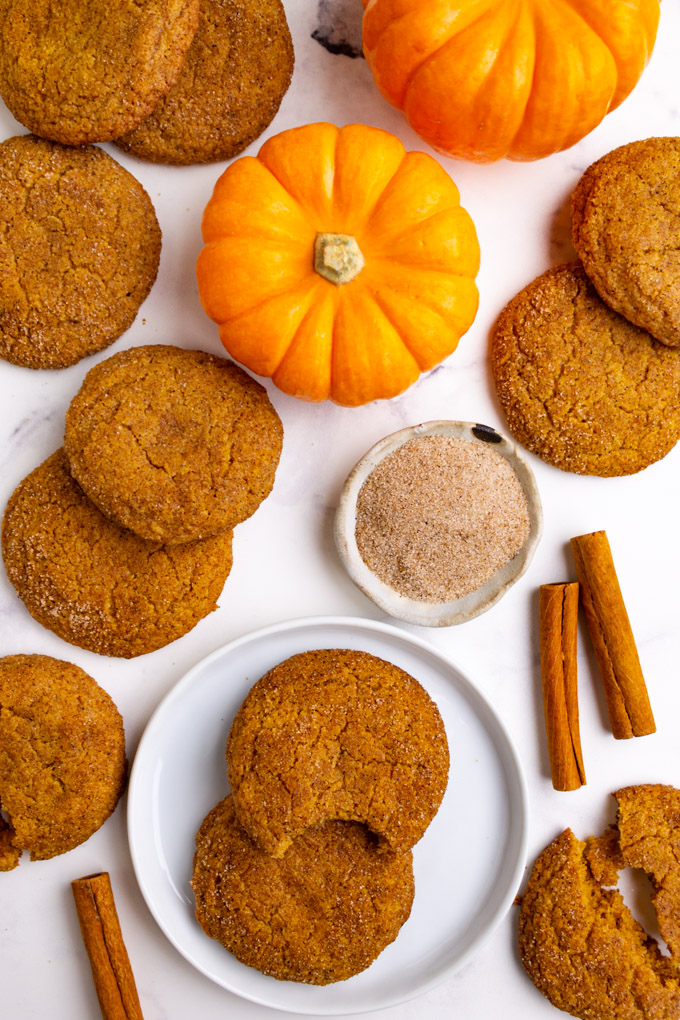 pumpkin snickerdoodle cookies on a white background with pumpkins in the background.