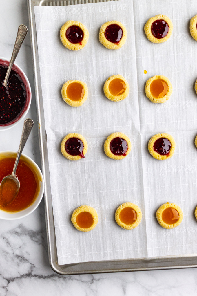 unbaked thumbprint cookies on a baking sheet filled with raspberry and apricot jam.