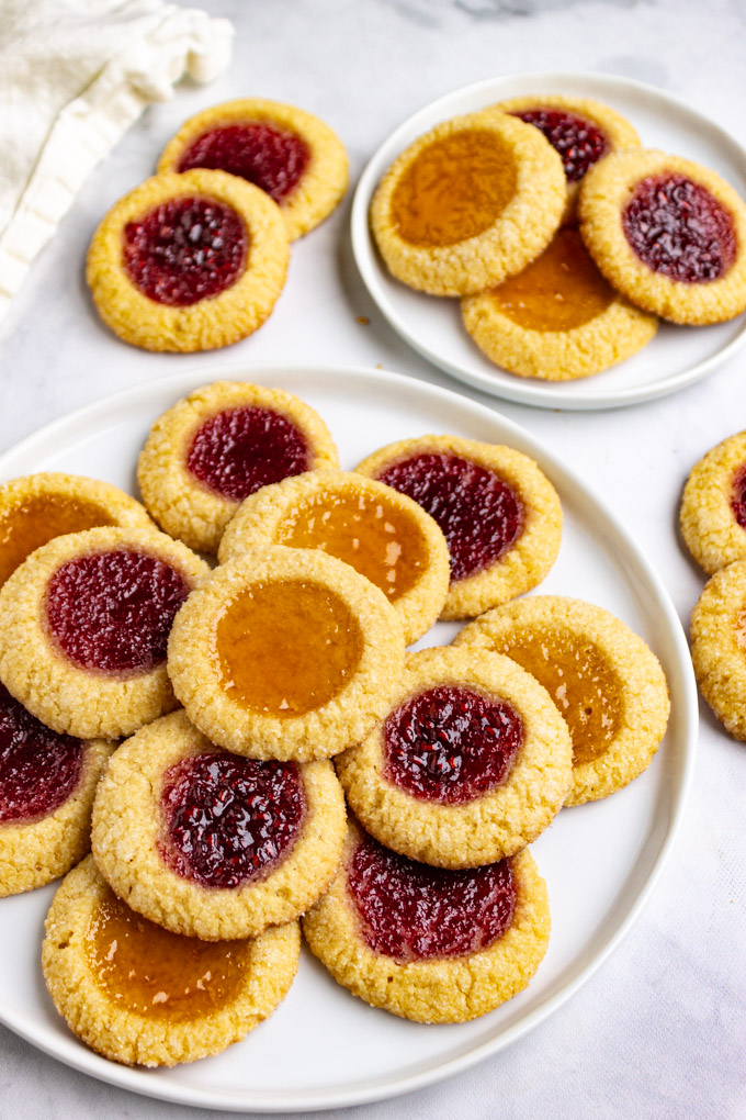 a close up angled shot of a stack of thumbprint cookies on a white plate, on a white background.