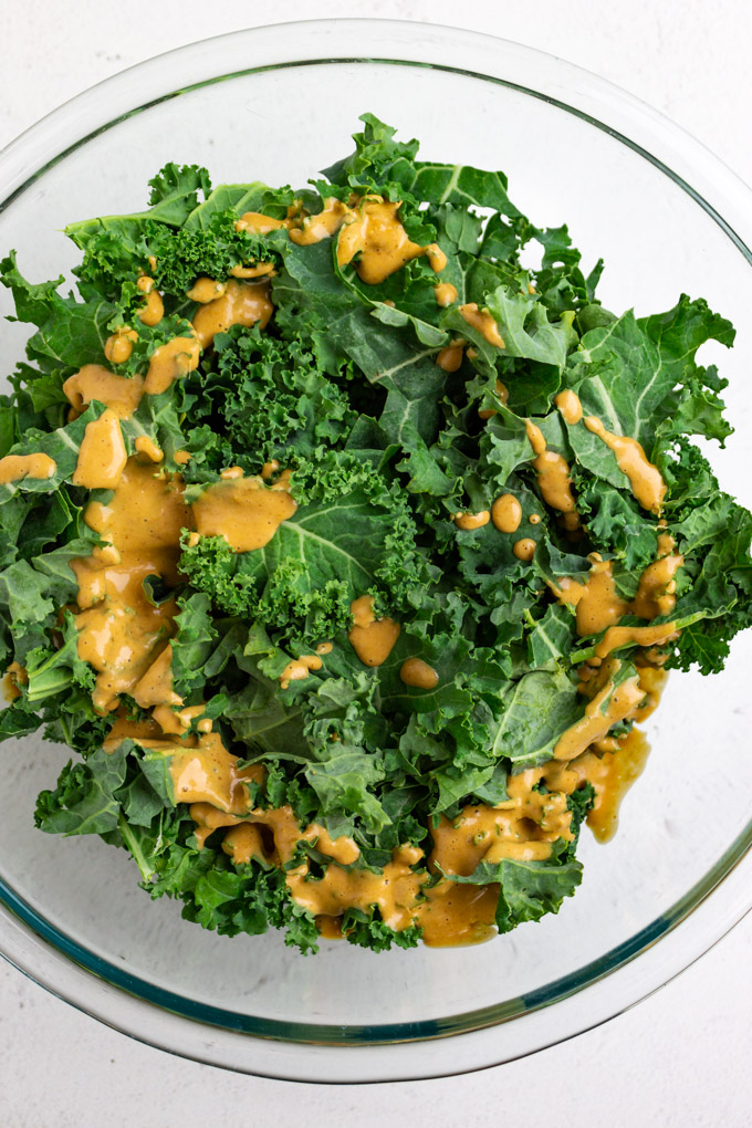 kale leaves in a mixing bowl with some of the peanut dressing over top.