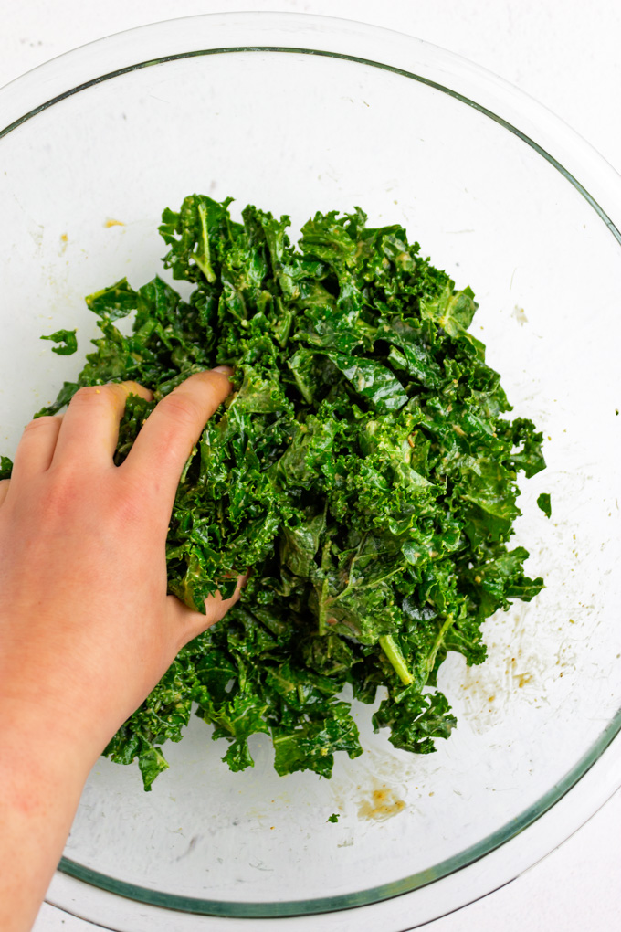 kale in a mixing bowl with a hand massaging it.