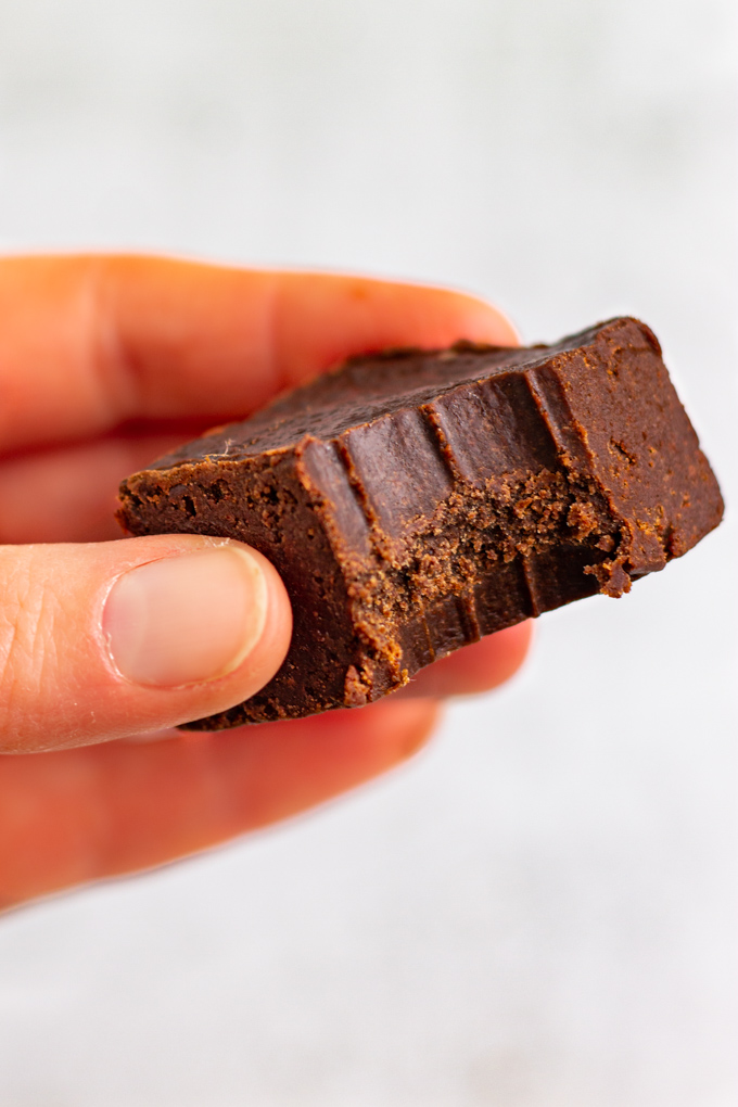 A closeup shot of a hand holding a piece of healthy chocolate fudge with a bite taken out of the fudge.