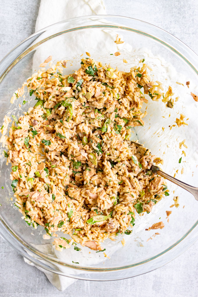 rice and salmon mixed together with mayo and green onions and cilantro in a mixing bowl.