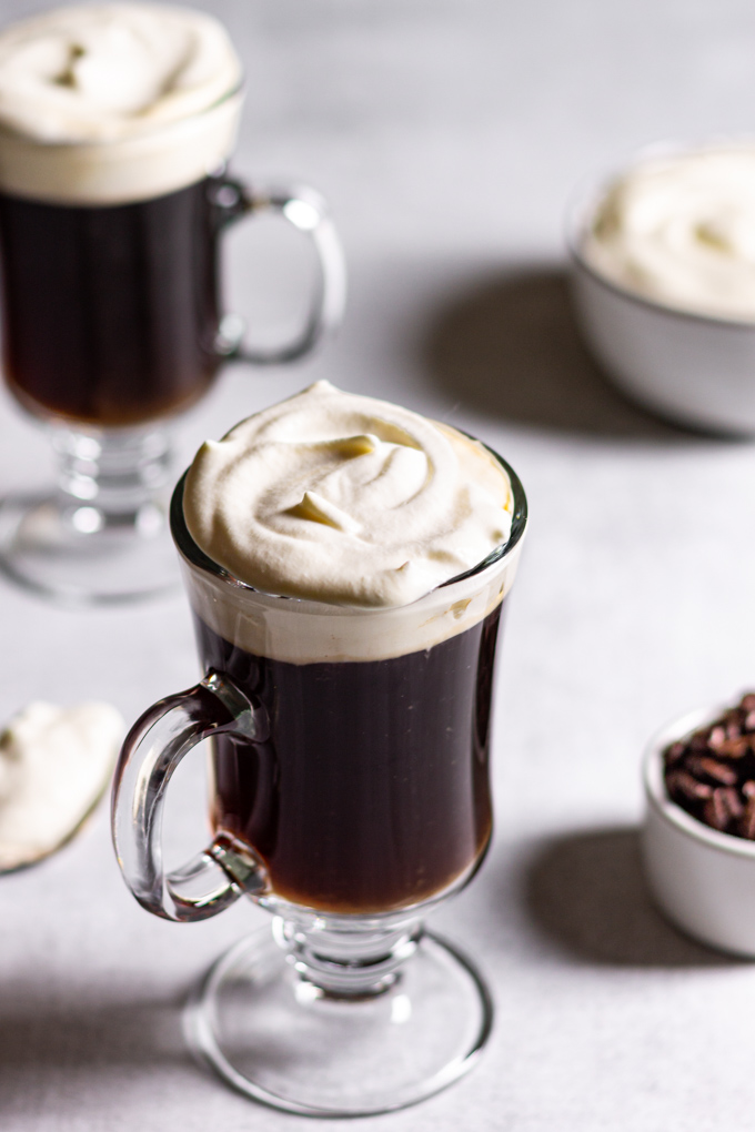 An angled shot of easy Irish coffee in clear mugs. A second drink is in the background.