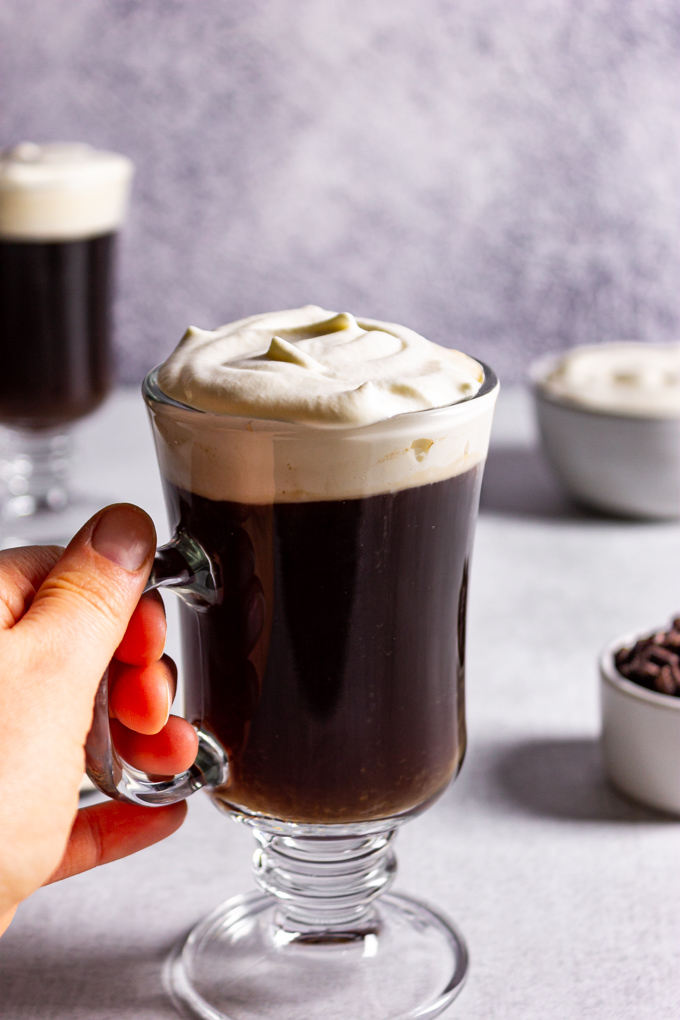 Easy Irish coffee in a clear glass mug with a hand holding the handle.