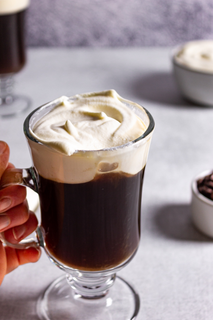 A mug of easy Irish coffee with a hand holding the handle and a drink has been taken out of the cream.