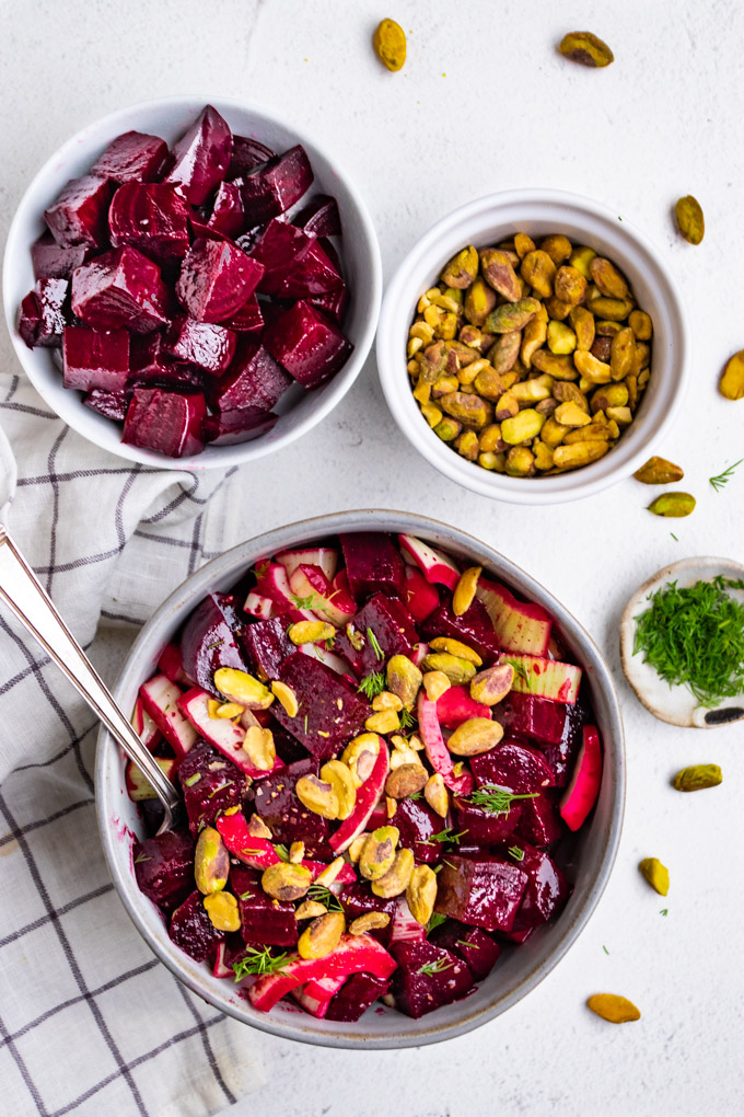 beet and fennel salad in a gray bowl, on a white background. A smaller bowl of beets are in the background, along with pistachios.