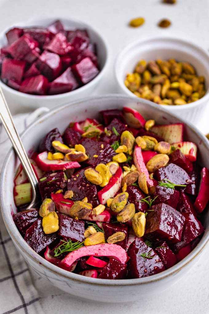 close up angled shot of beet and fennel salad in a gray bowl. A smaller bowl of beets, and pistachios are in the bacground.