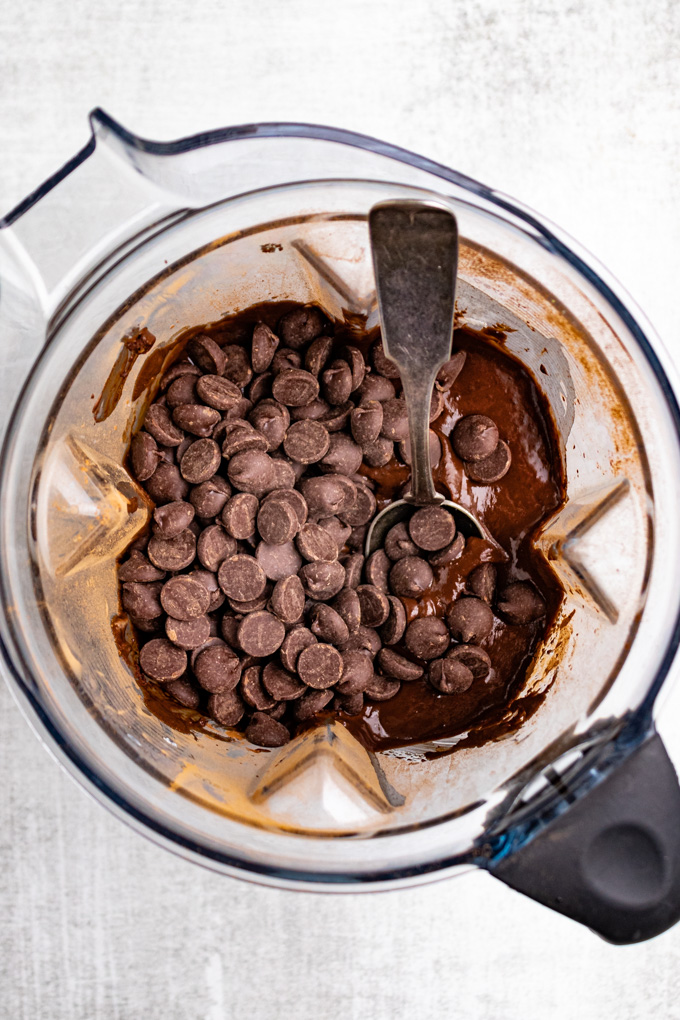 chocolate muffin batter in a blender with chocolate chips being stirred in by a spoon.