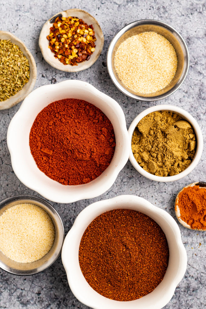 Spices in different bowls - chili powder, smoked paprika, cumin, garlic powder, onion powder, cayenne pepper, dried oregano, and red pepper flakes.