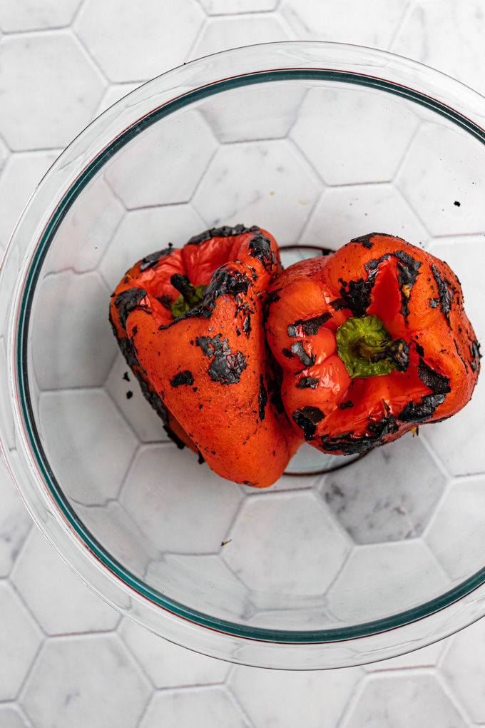 Peeled roasted red peppers in a clear mixing bowl, on gray hexagon tiled countertop.