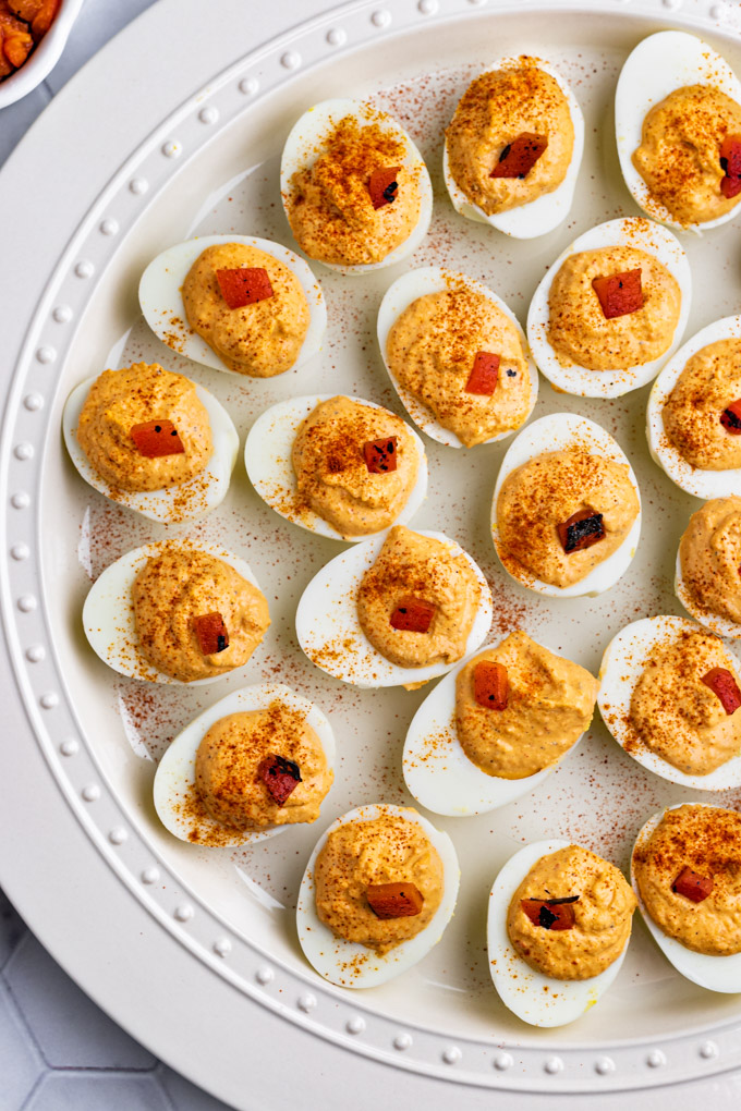 A platter of roasted red pepper deviled eggs with paprika sprinkled on tip of the eggs and a slice of roasted red pepper too.