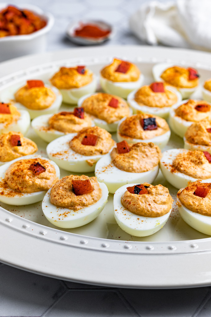 Closeup, angled shot of roasted red pepper deviled eggs. The eggs are on a large white platter.