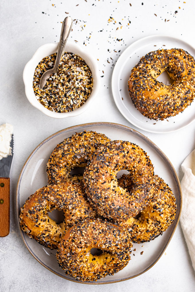 A plate of bagels with everything bagel seasoning on the bagels. A small white bowl of everything bagel seasoning is in the background.
