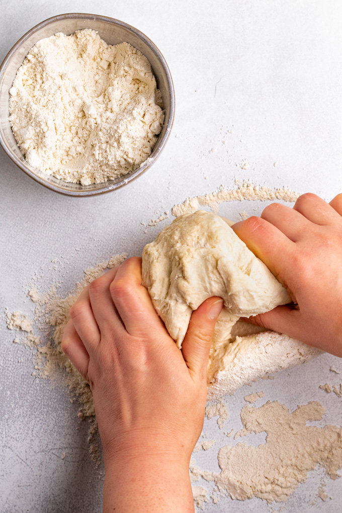 Hands kneading the bagel dough, with a bowl of flour in the corner.