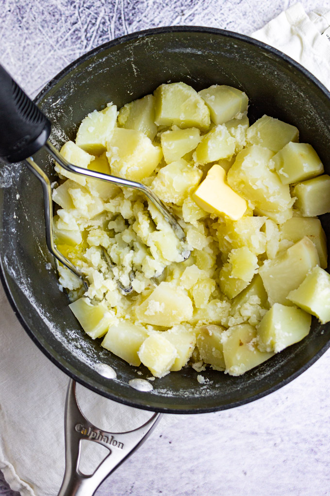 cooked potatoes in a pot, being mashed. 
