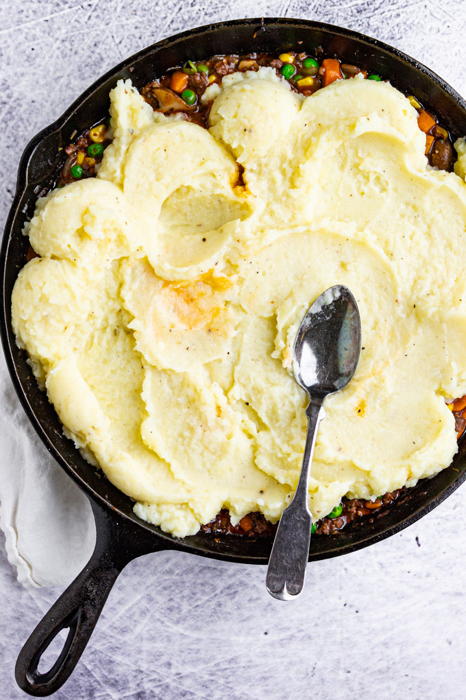 shepherd's pie in a cast iron skillet with mashed potatoes being spread on top.