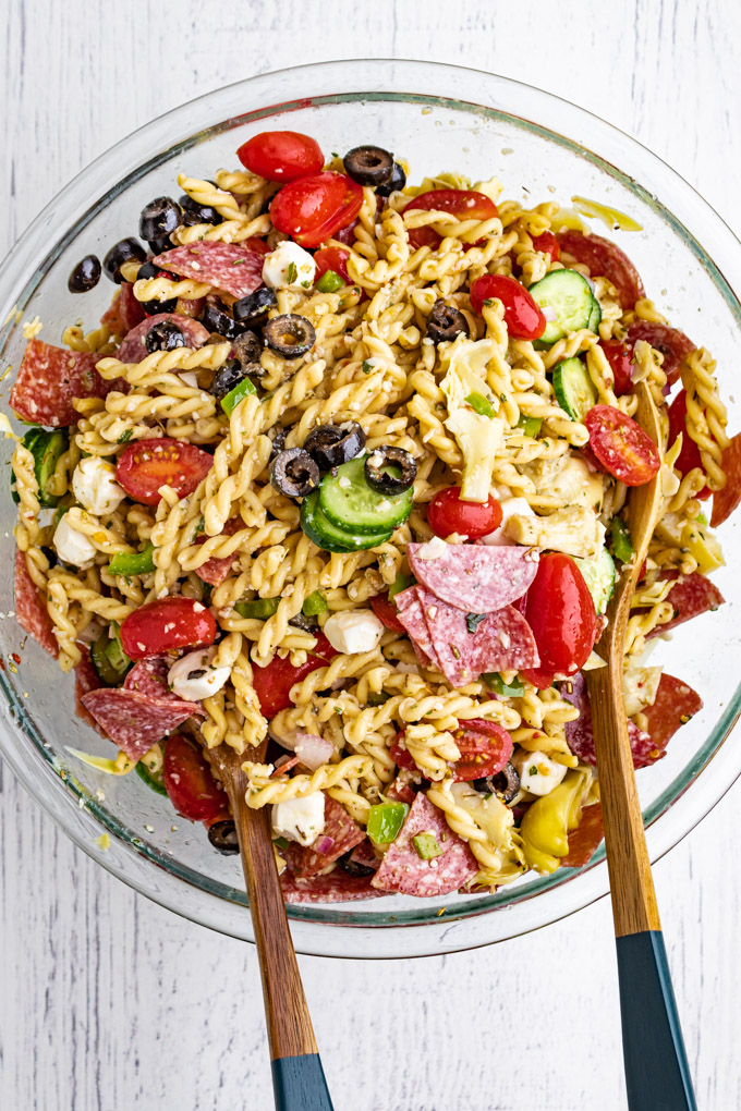 Italian pasta salad in a mixing bowl, just tossed. Wooden salad spoons are in the mixing bowl.