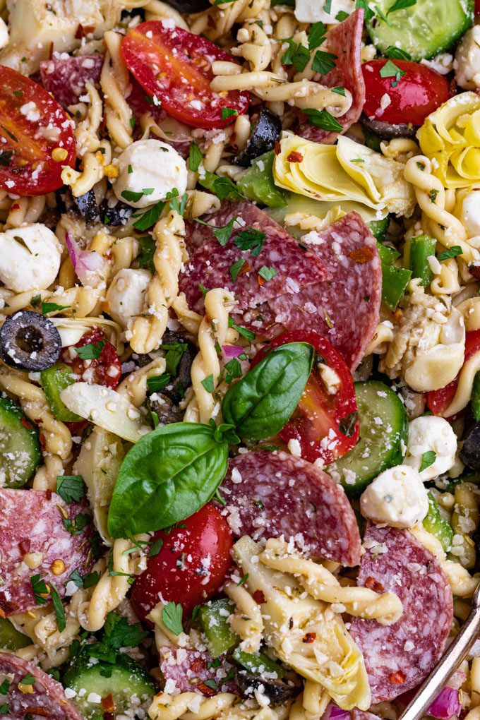 A macro close up shot of Italian pasta salad with salami. The serving bowl it's in is not visible. Fresh basil is the center of the photo.