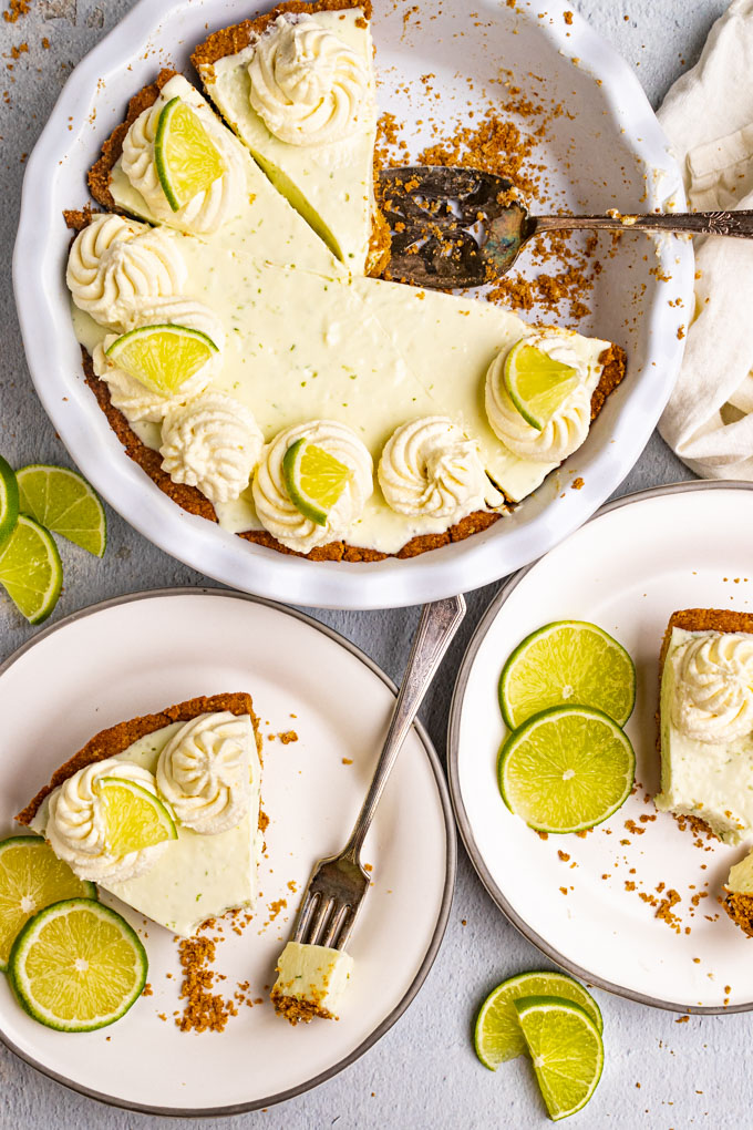 Overhead shot of the best key lime pie. 2 slices of pie are removed from the pie, and on plates. Bites are taken out of the pies. The remaining pie in the pie plate is the background.