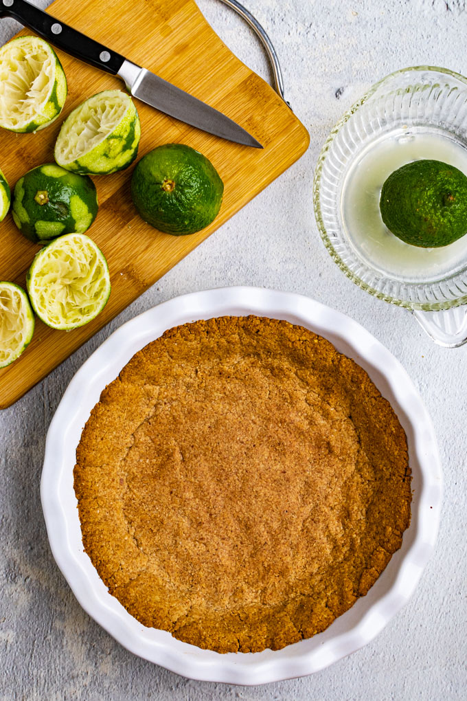 Overhead shot of gluten free graham cracker crust in a pie plate, with squeezed limes in the background.