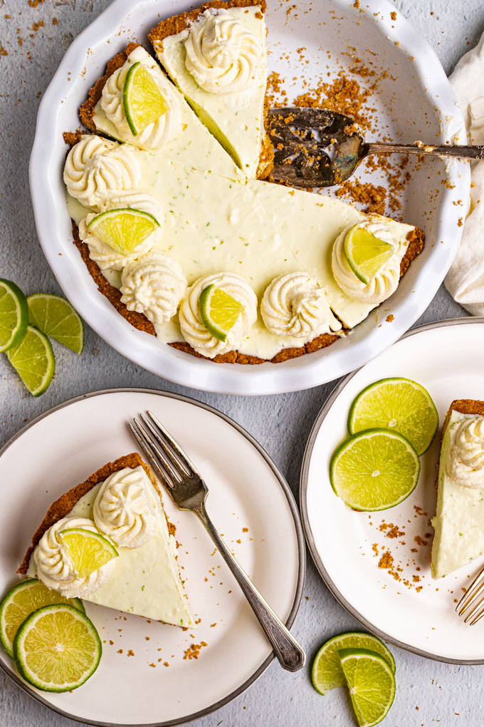 Overhead shot of the best key lime pie. 2 slices of pie have been removed from the pie and are on plates. The remaining pie is in the background with a pie server.