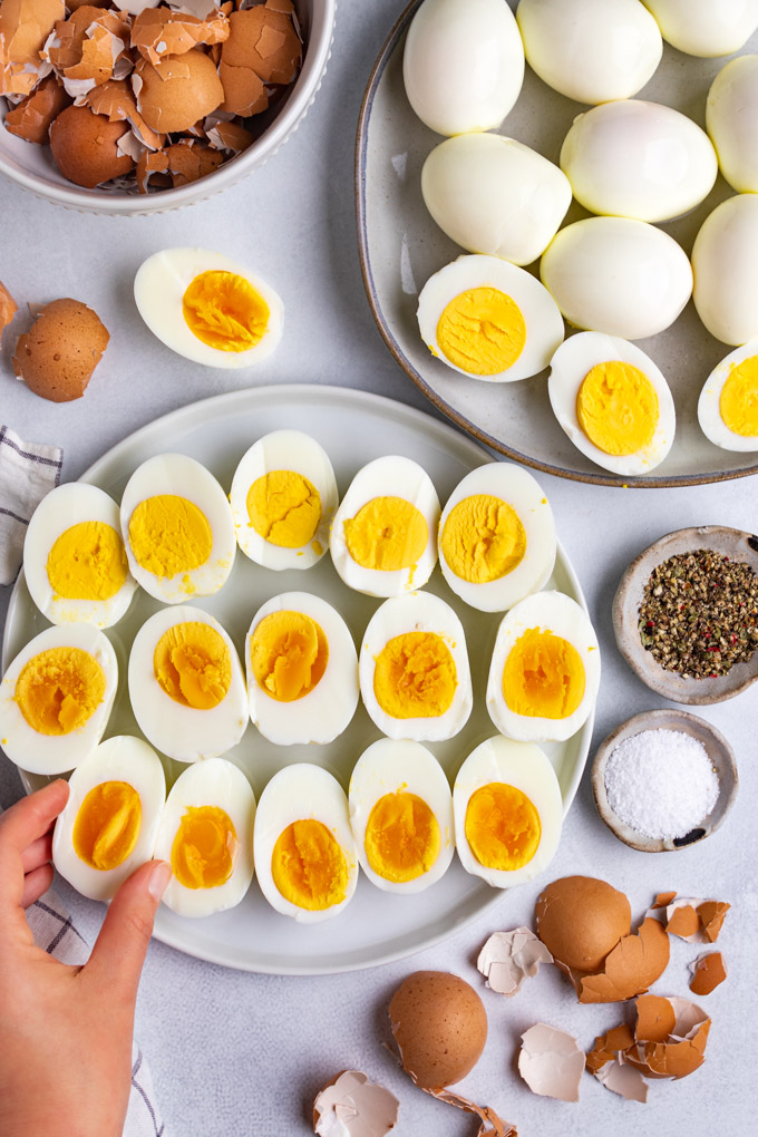 Instant pot hard boiled eggs are on a plate, sliced in half. A hand is about to pick up one of the eggs.