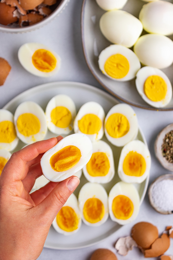 Instant pot hard boiled eggs. Eggs are sliced in half on a plate. The 2 minute egg is being held up by a hand.