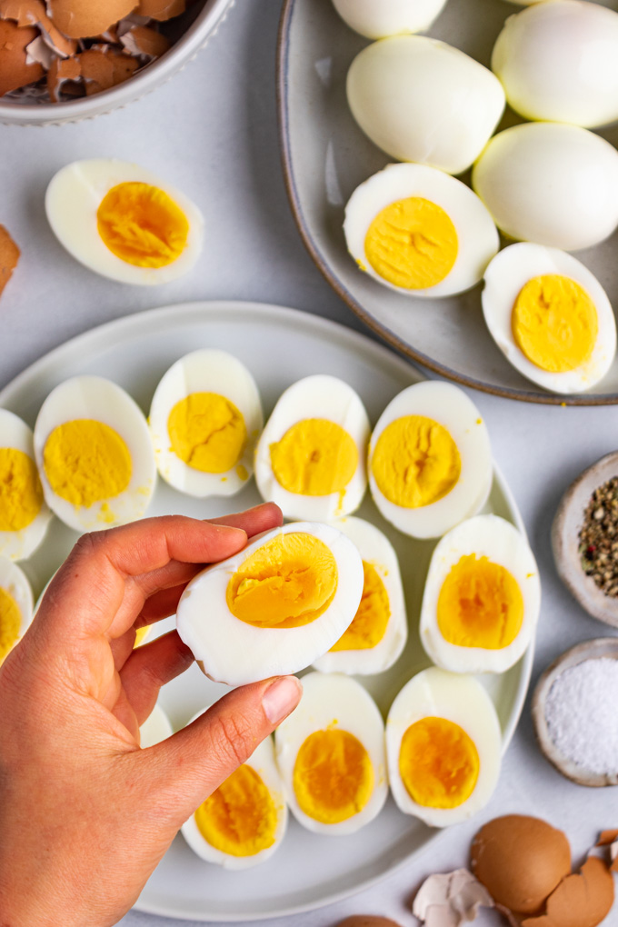 A plate of instant pot hard boiled eggs are sliced in half, on a plate. One 3 minute egg is being held up by a hand.
