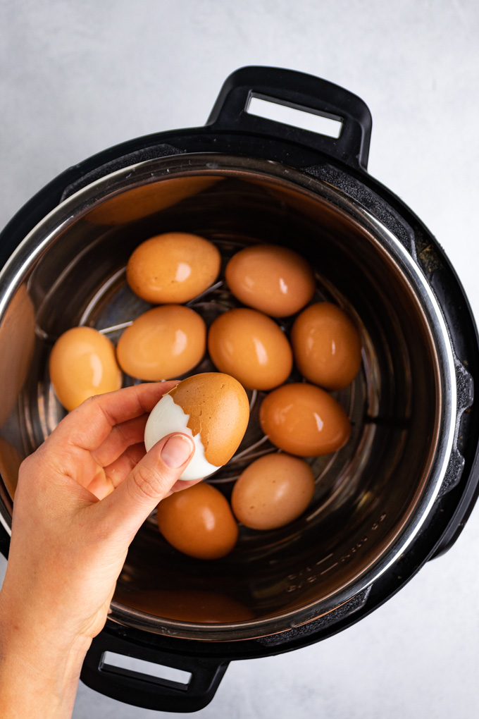 Hard boiled eggs in an instant pot. One egg is half peeled, it is being held up by a hand. Instant pot hard boiled eggs.