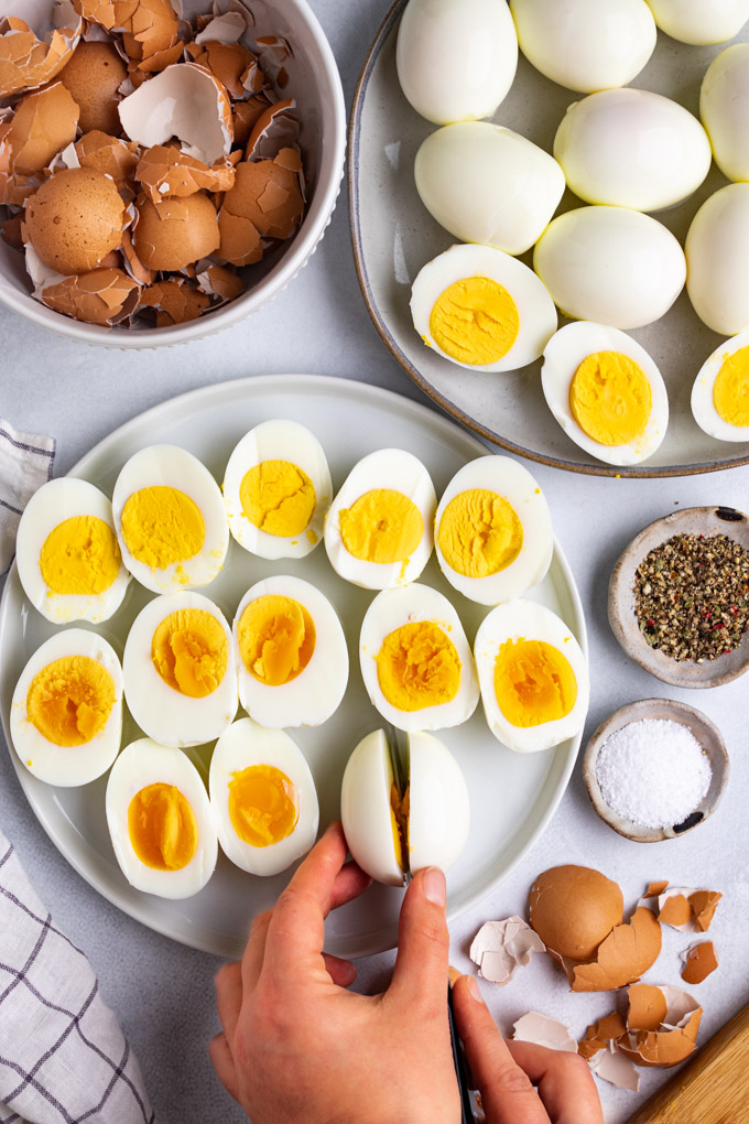 Instant pot hard boiled eggs are sliced in half on a plate. One egg is being sliced in half.