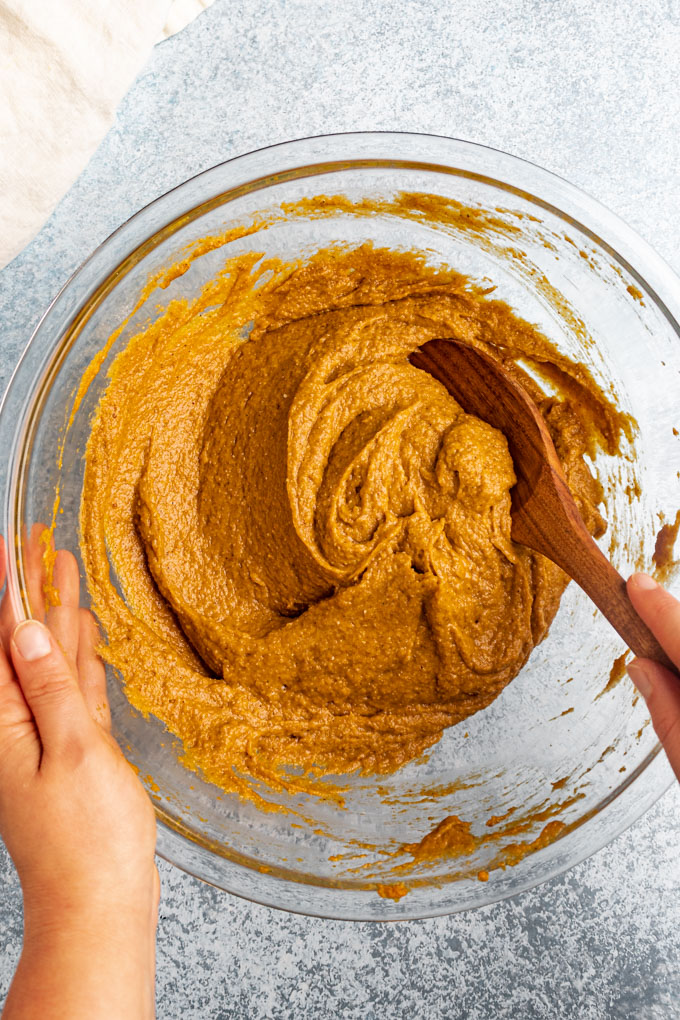 Pumpkin bread batter is being mixed in a bowl with a wooden spoon.
