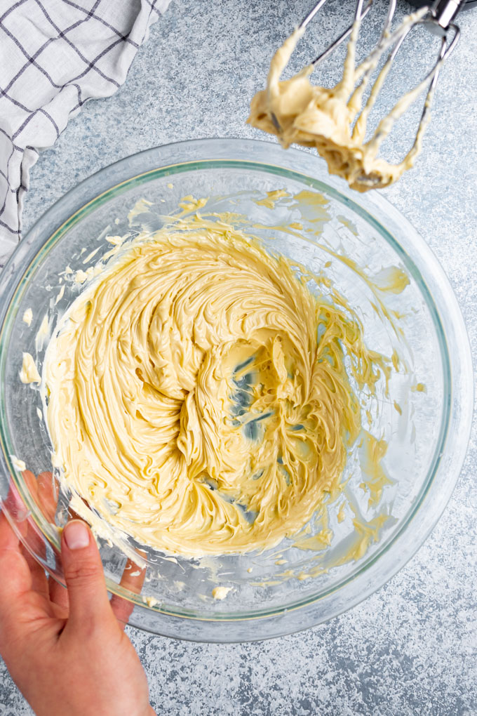 Whipped maple butter in a mixing bowl, on a light blue background. The beaters of a hand mixer are in the corner.