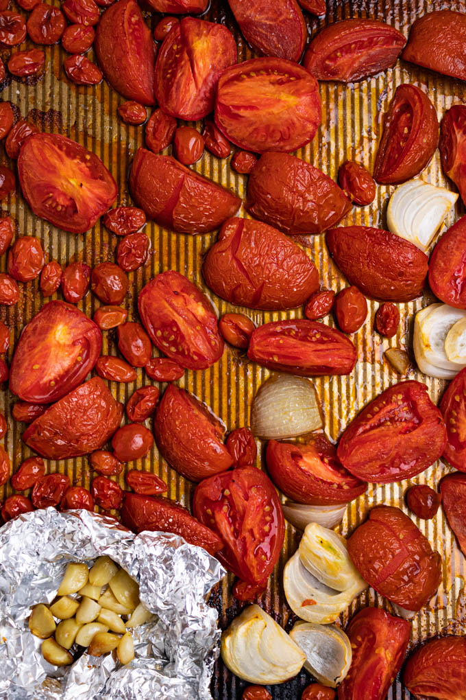 A sheet pan full of roasted tomatoes, and onions. Along with a foil packet of roasted garlic cloves.
