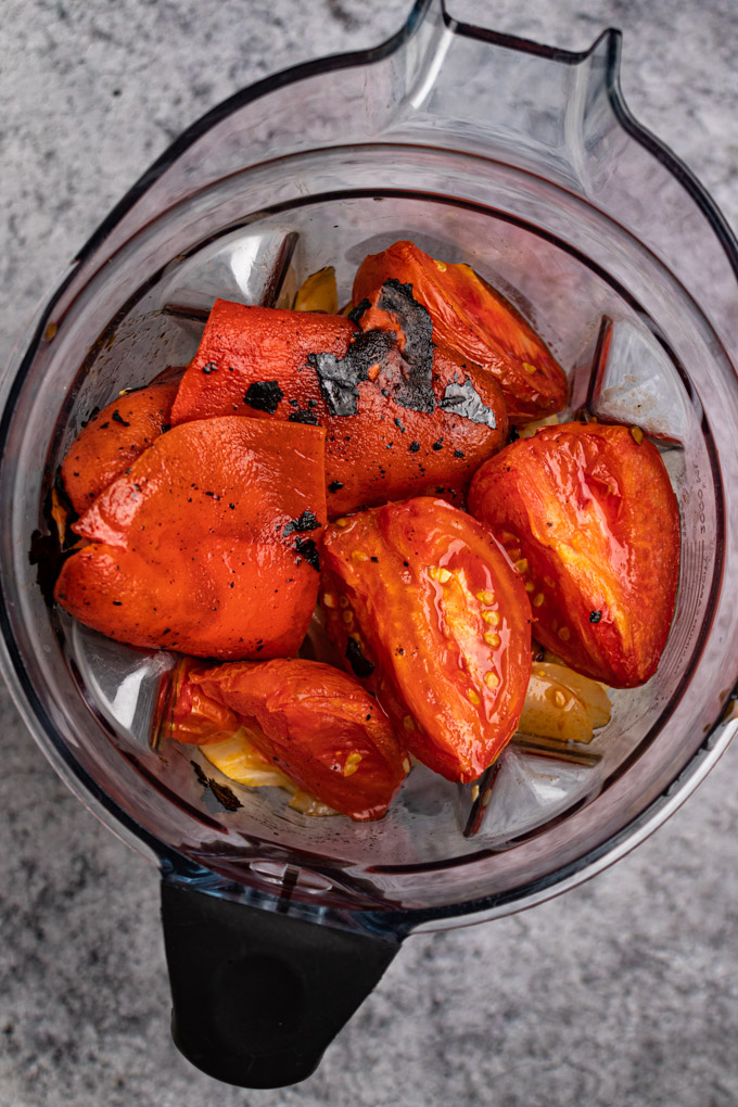 Roasted tomatoes, and roasted red peppers are in a blender, waiting to be blended in to a soup.