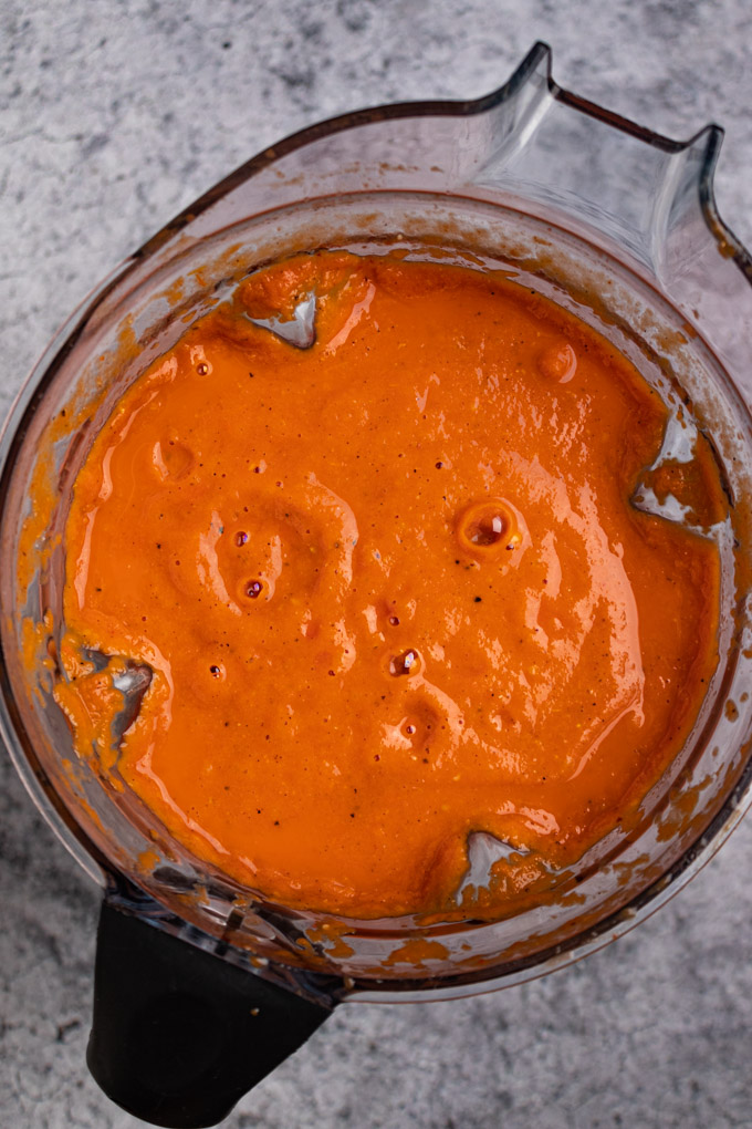 Roasted tomato and red pepper soup is in a blender, blended into a smooth soup.