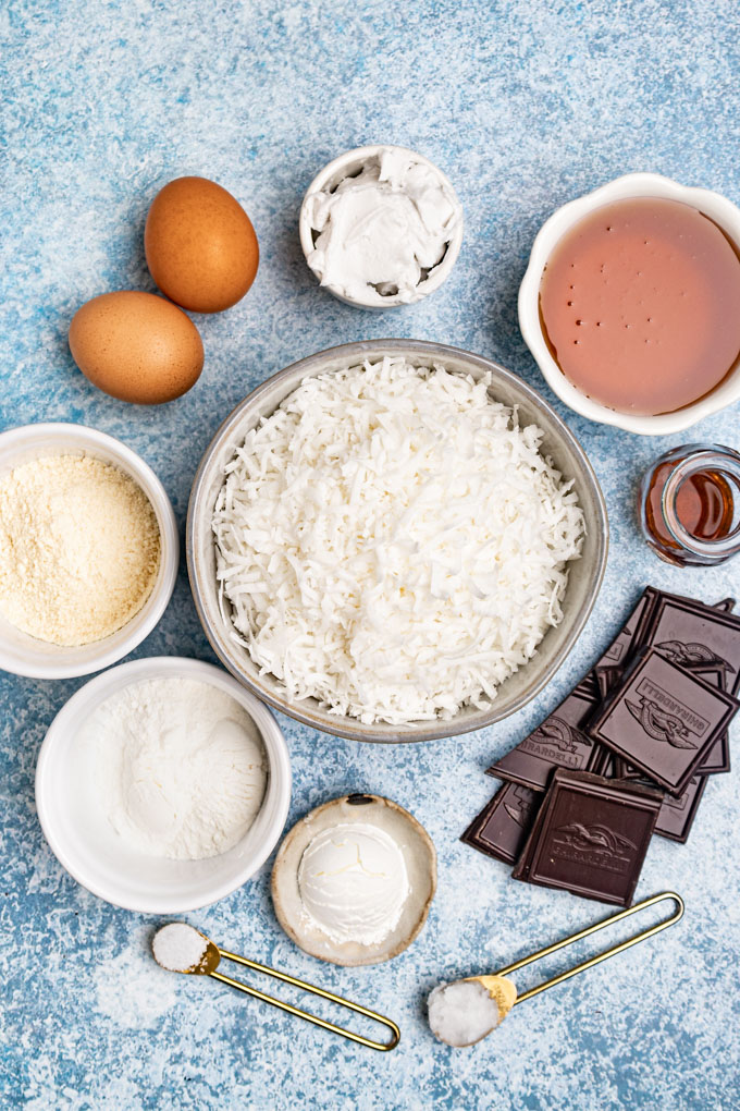Ingredients portioned out into bowls: shredded coconut, eggs, dark chocolate, honey, flour, and coconut cream.