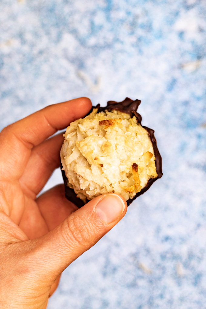 A close up of a hand holding a coconut macaroon with a light blue background.